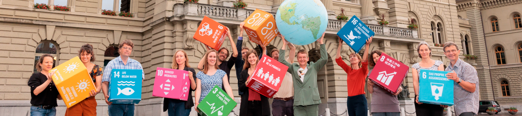 Un groupe de personnes se tient sur la Place fédérale avec de grands cubes SDG et un grand globe terrestre.